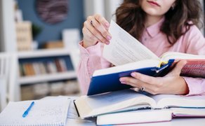 Bild von einer Frau, die in einer Bibilothek sitzt und Bücher studiert