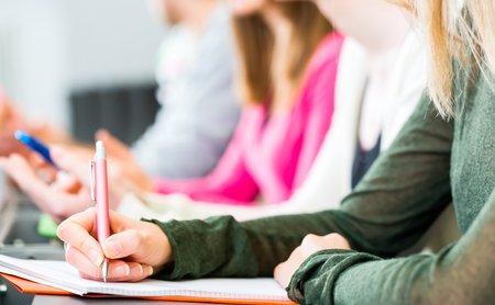 Nahaufnahme von einer Person, die im Unterricht sitzt und mitschreibt