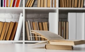 Bild von einem Buch auf einem Tisch und einem Bücherregal im Hintergrund